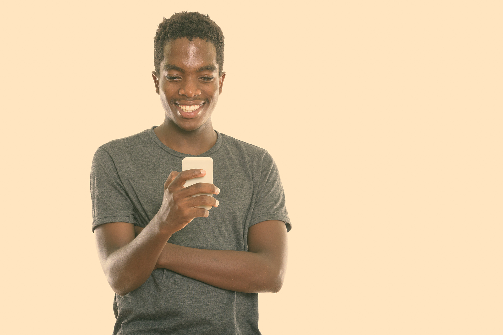 Attractive young black man with a t shirt smiling looking at his phone against a plain background.