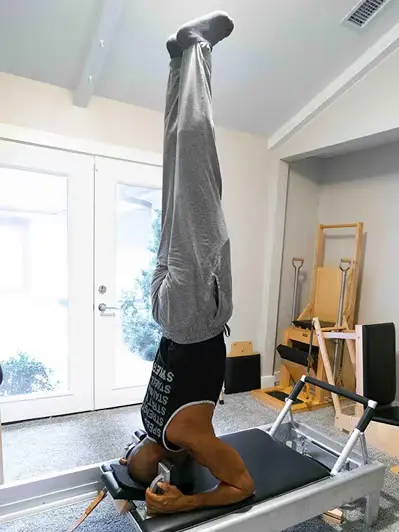Chris Robinson upside down on the Gratz Pilates Reformer. Ladder barrel and Spine Corrector in the background