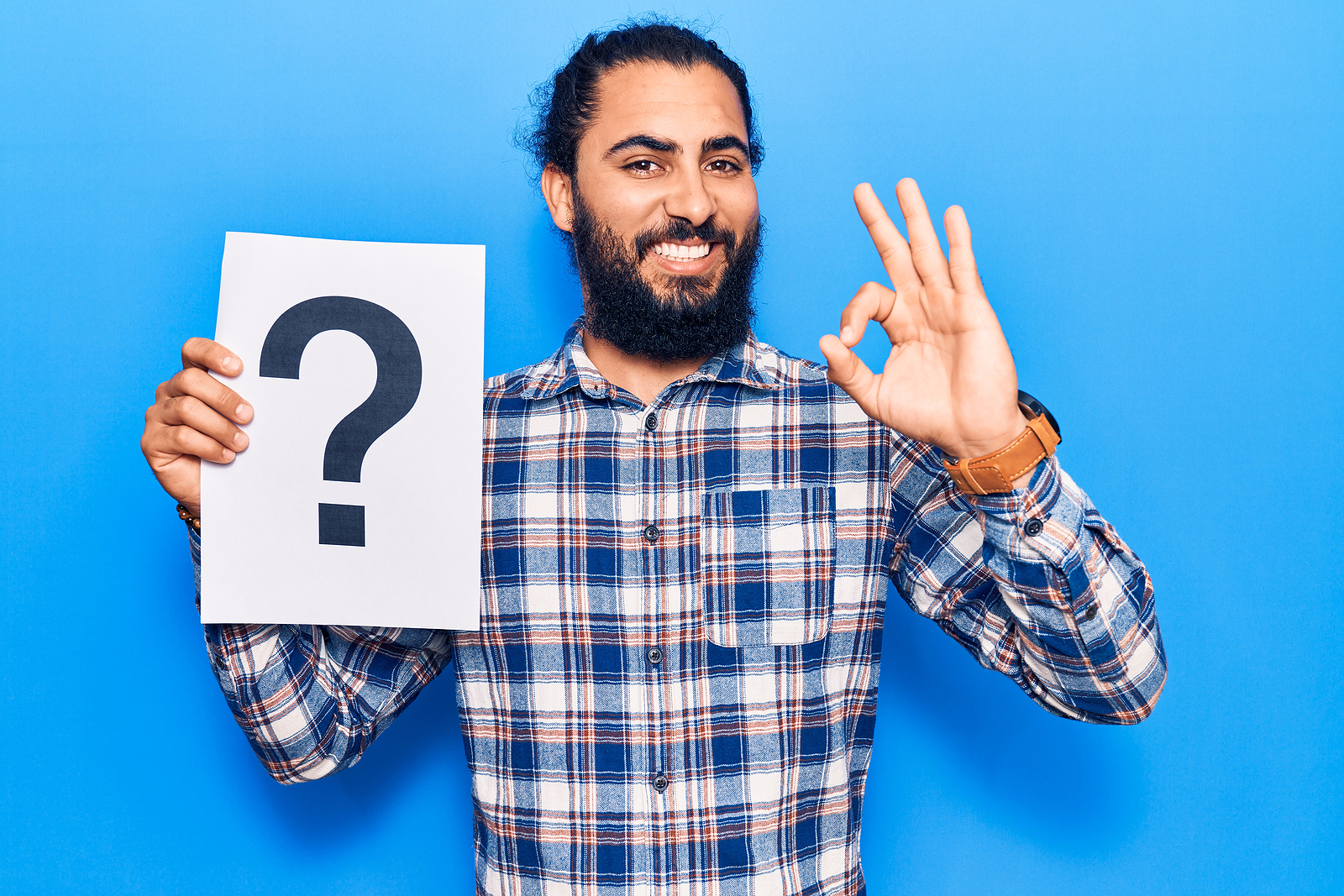 Young arab man holding question mark doing ok sign with fingers, smiling and friendly.