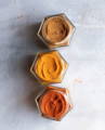 Three open hexagonal glass spice jars are filled with orange and brown ground spices.