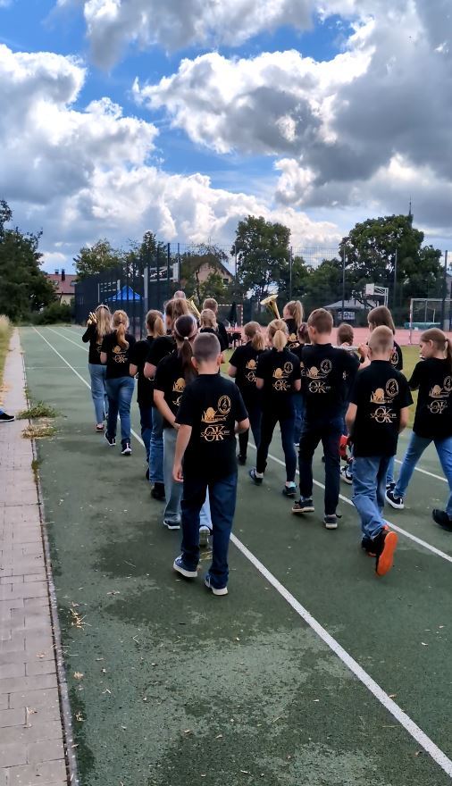 Viele Kinder in einheitlichen T-Shirts marschieren über einen Sportplatz. 