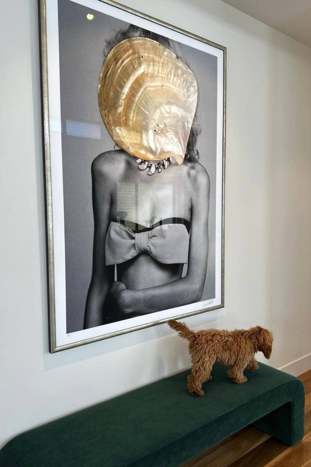 'Mother of Pearl' by Dina Broadhurst - A framed black and white fashion photograph embellished with a collaged shell over the figures face, captured in a home with bench seat beneath hanging artwork.