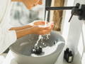 woman washing her face at sink with skincare products