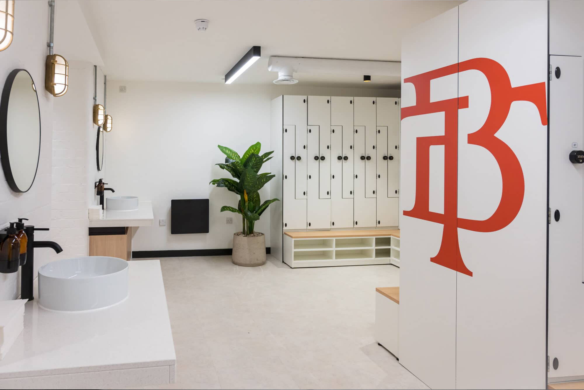 An image of the interior lockers inside the historic Manchester Tootal Building with the logo printed in red vinyl on the side of the lockers. There is a large plant and a few sinks.