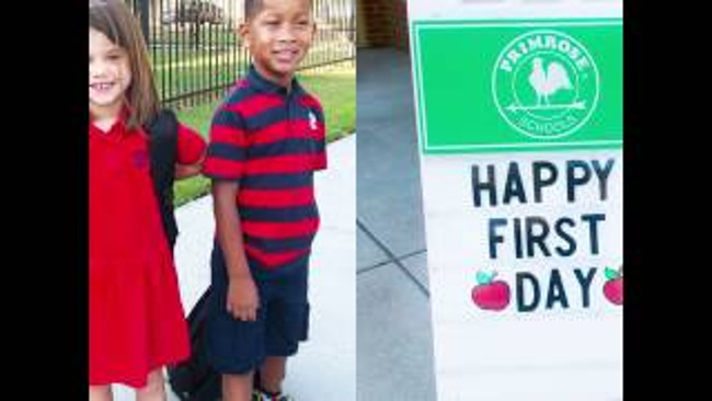 Two young and smiling Primrose students stand next to a happy first day of school poster