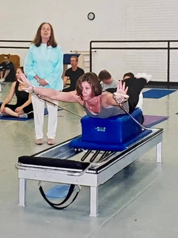 Romana teaching Dana on the reformer. Dana is laying on top of reformer box 