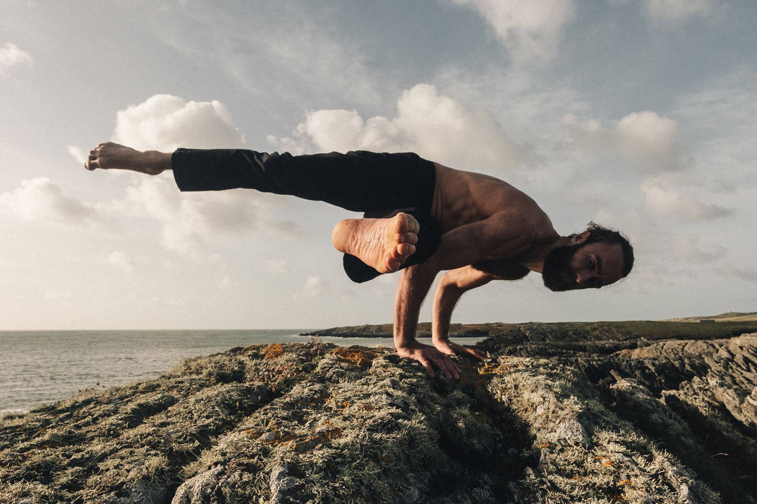 Leo Oppenheim balancing on a rock wearing So We Flow... Flow Trousers in Navy.