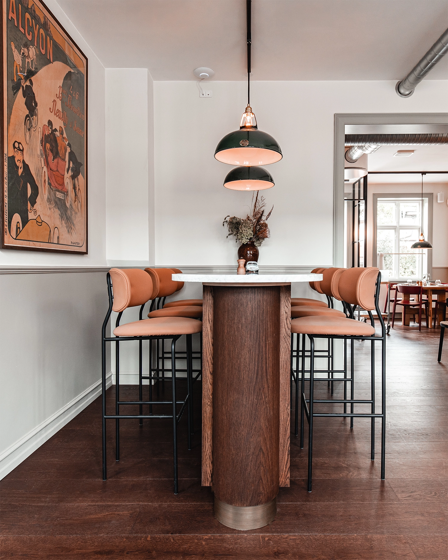 Two large Green Coolicon Pendant lampshades hanging above a bar island inside a restaurant with white walls. 
