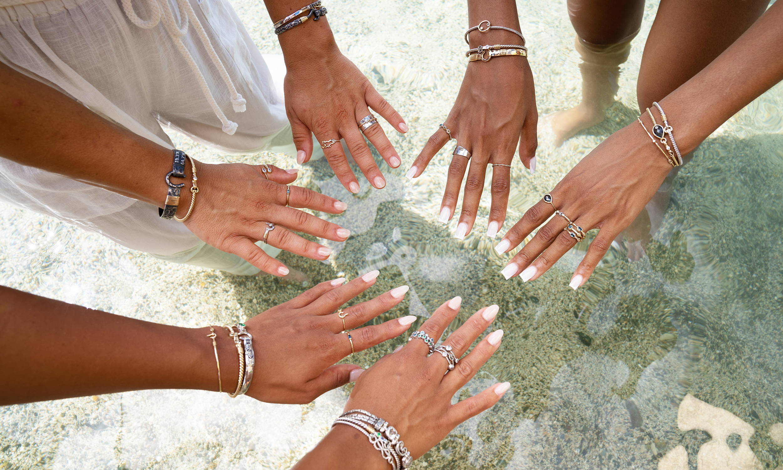 Three peoples hands put together over a the ocean showing off their Vibe Jewelry.