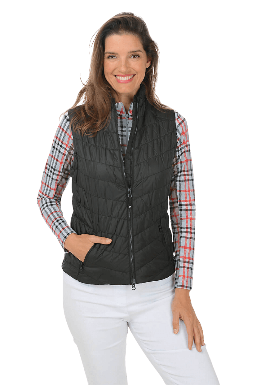 A woman in a plaid long sleeve shirt, a black puffer vest, and white pants