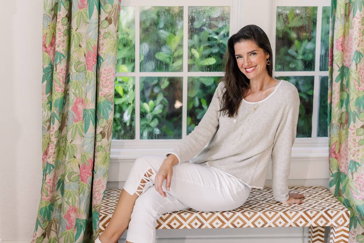 A woman wears a tan cotton crewneck lounging by a sunny window.