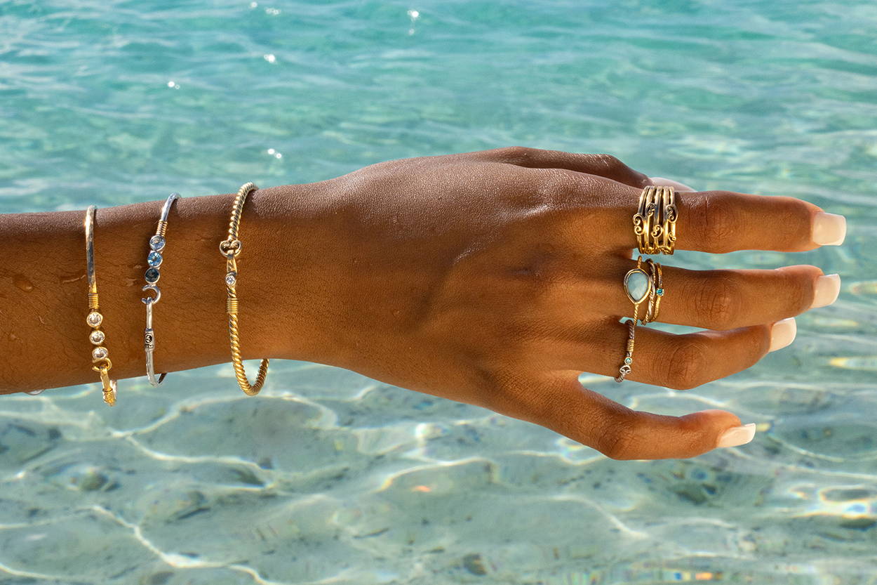 Hand and arm wearing Vibe Jewelry with ocean water in the background.