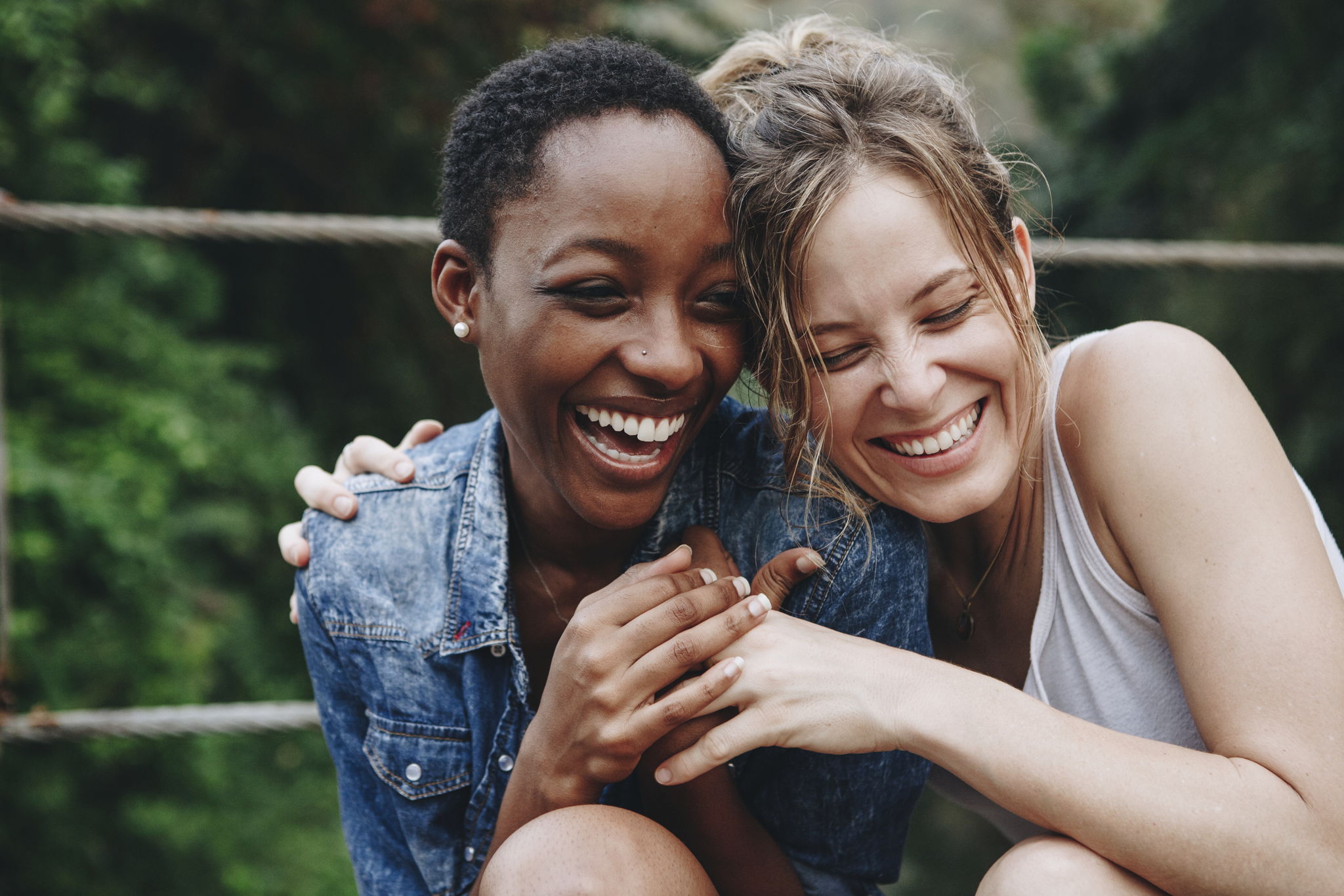 Two multiracial women laugh together while sitting close together.