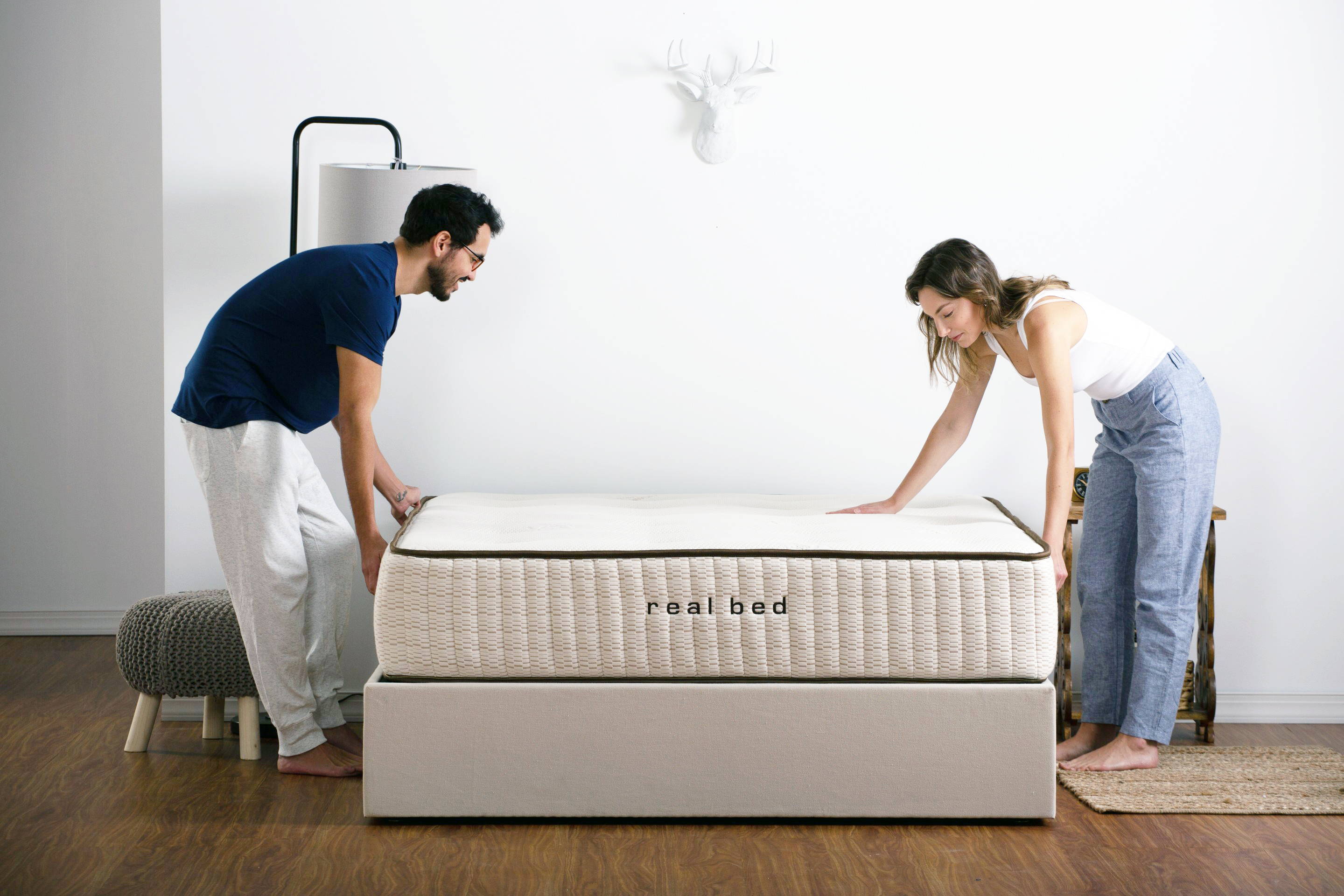 Man and woman making a bed in stylish white bedroom. Image