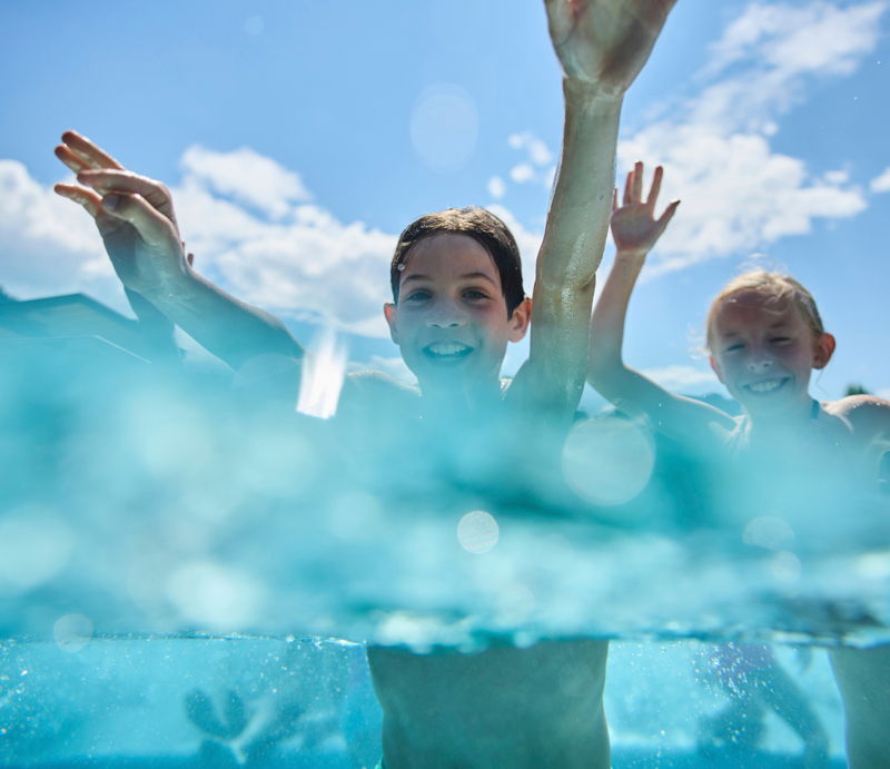 Kinder beim Schwimmen im Freibad im Kleinwalsertal bei sonnigem Wetter.