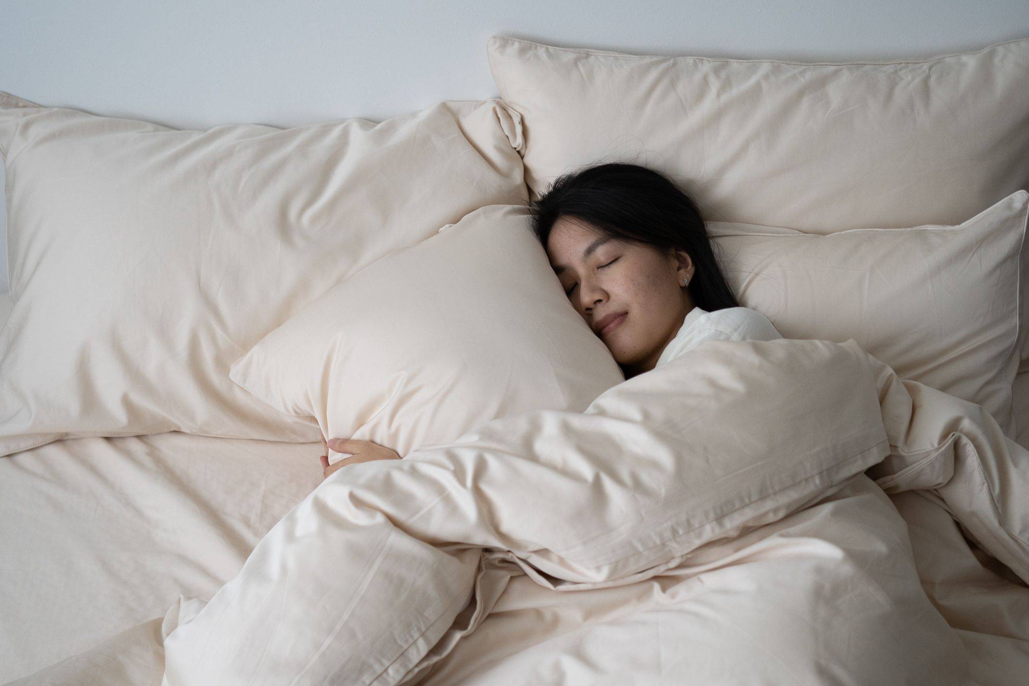 A woman sleeping peacefully in bed featuring Weavve's cotton bed sheets in cream colour