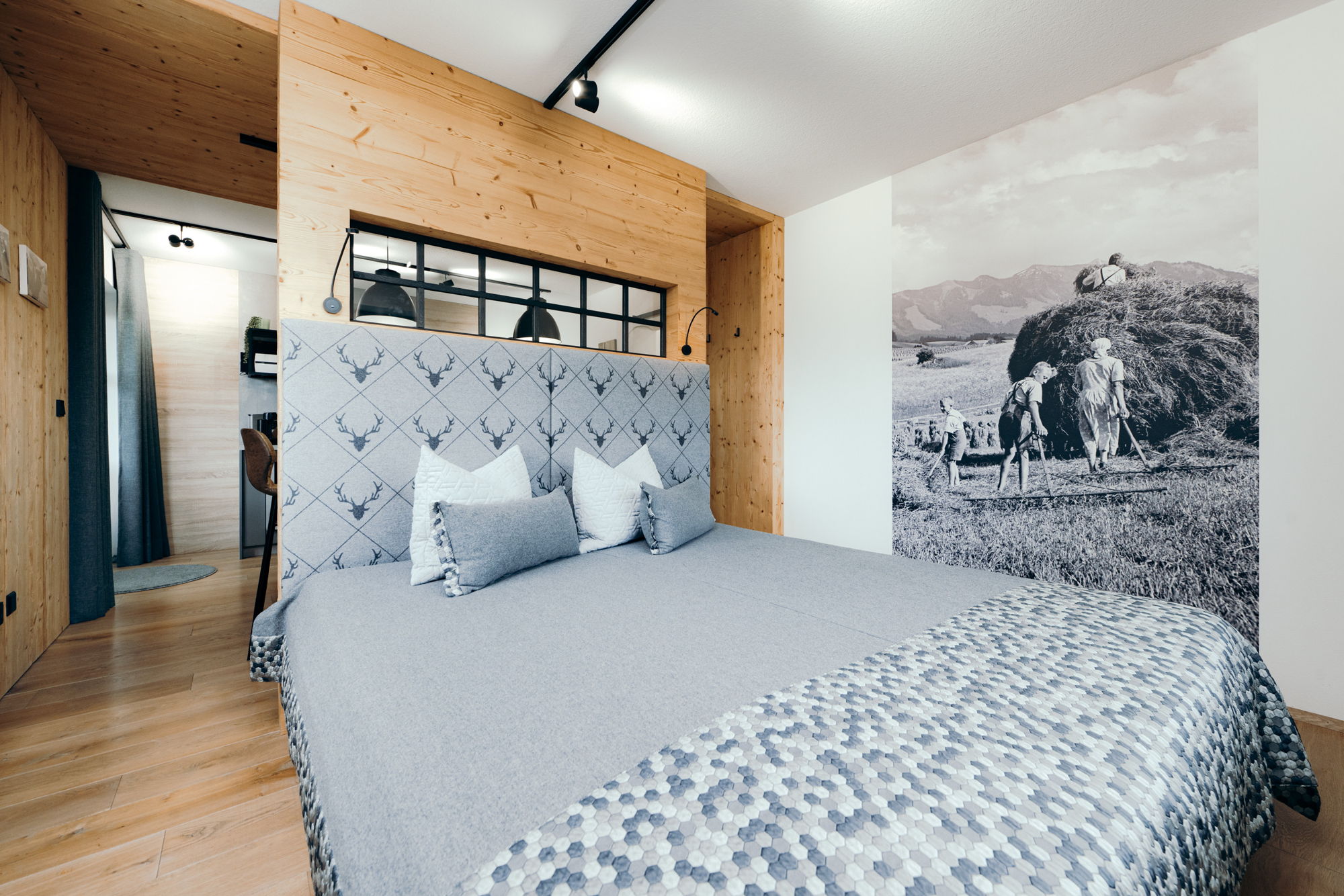 Ein grau bezogenes Doppelbett, im Hintergrund ein schwarz-weiß Bild von Bauern bei der Arbeit.