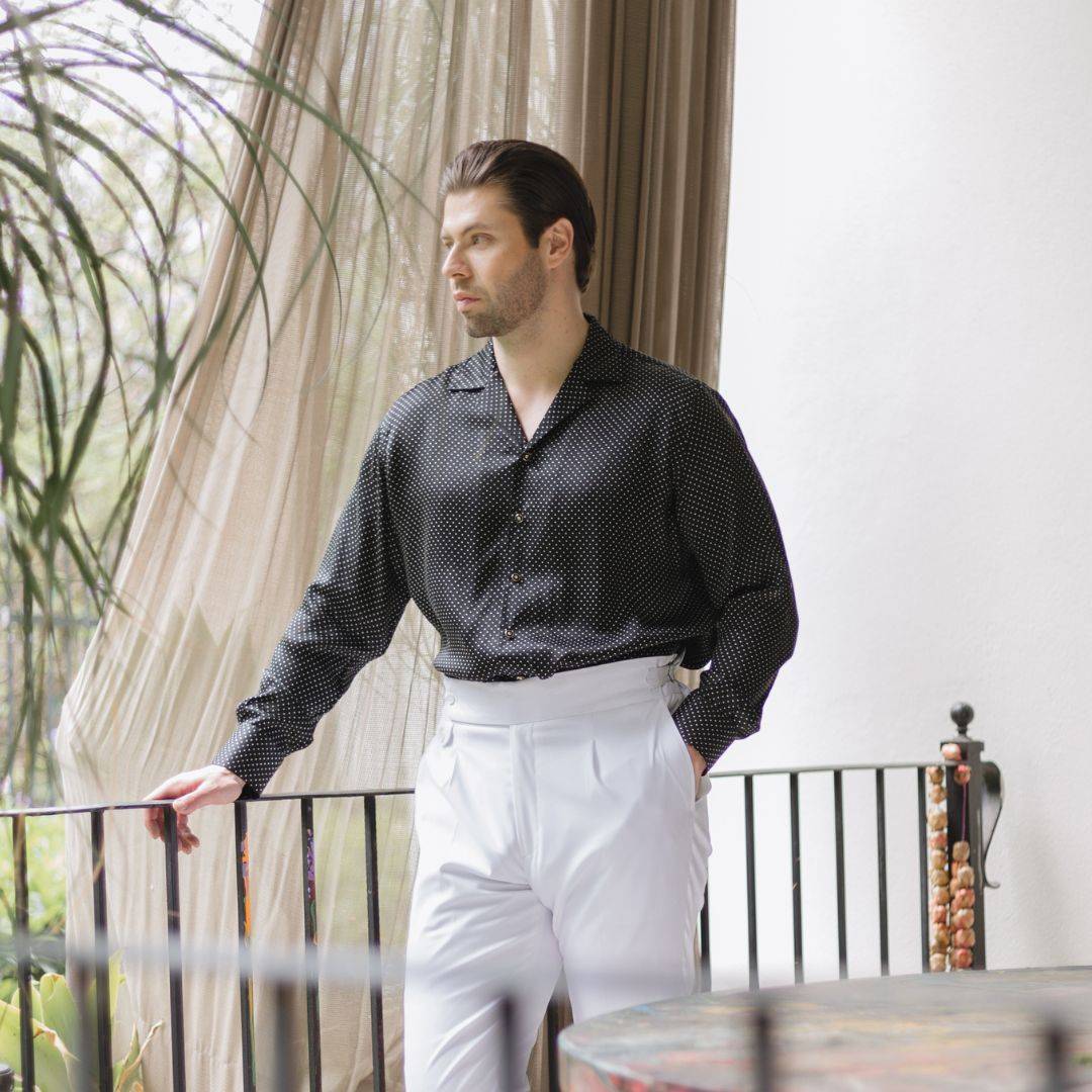 model standing outside wearing white high rise pants and a long sleeve black dotted silk shirt from 1000 kingdoms