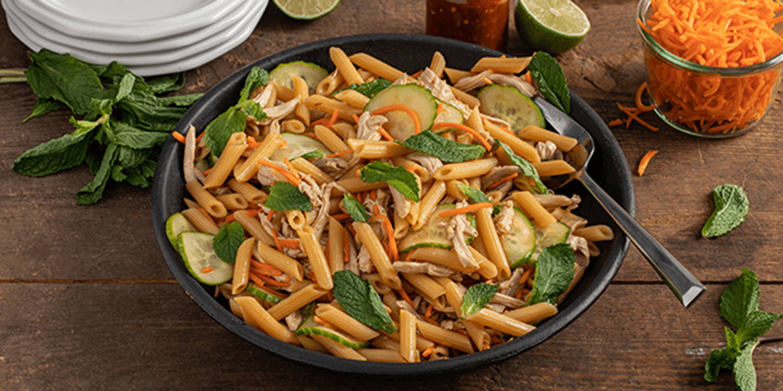 Bowl of pasta salad with cucumber, chicken, carrot, and mint.