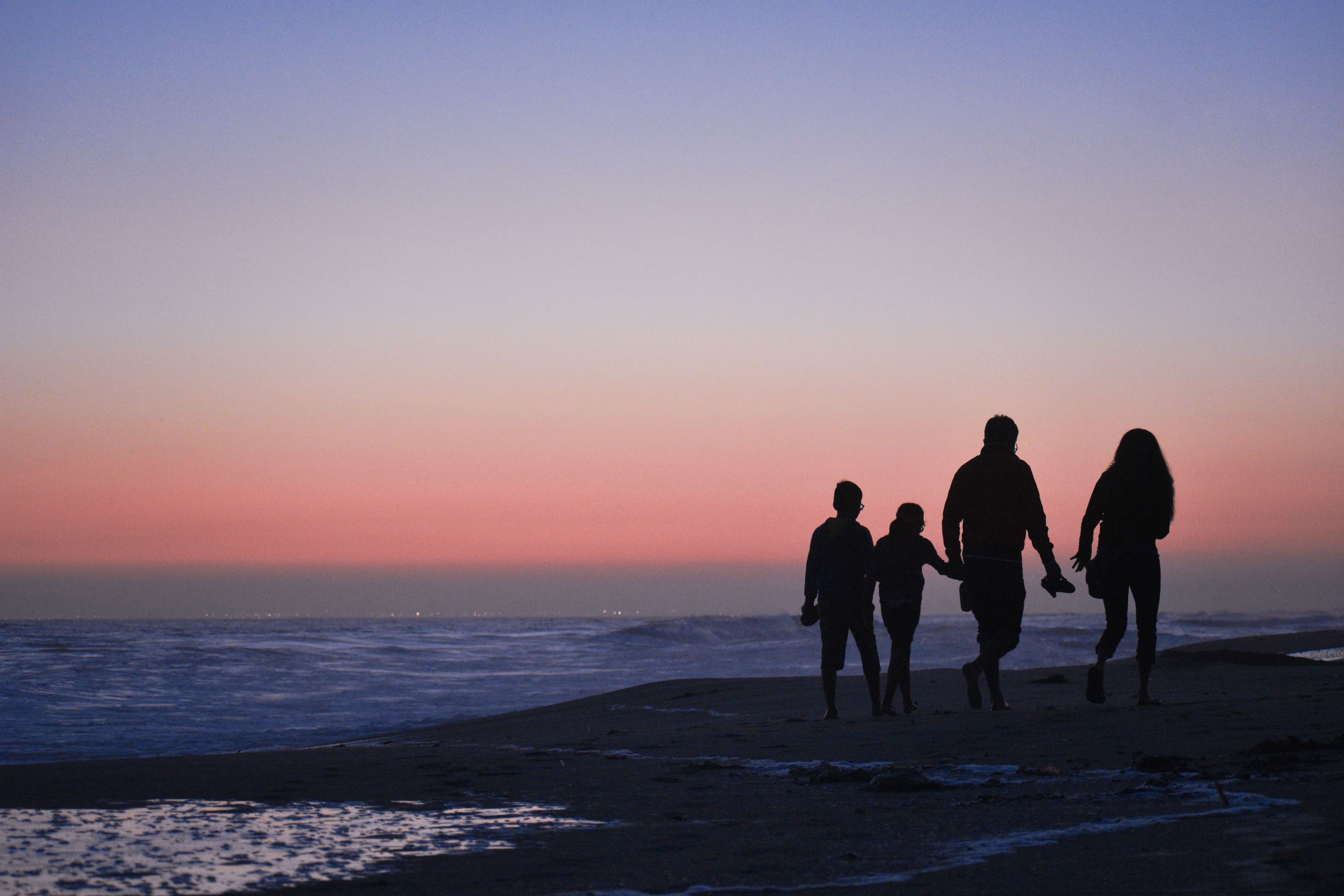The silhouette of a family walking on the beach while the sun is set.