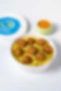 A white container of fish ball biryani topped with golden fried balls, served with a side of tangy sauce.