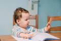 Cute chubby baby sitting at the table and holding pencils.