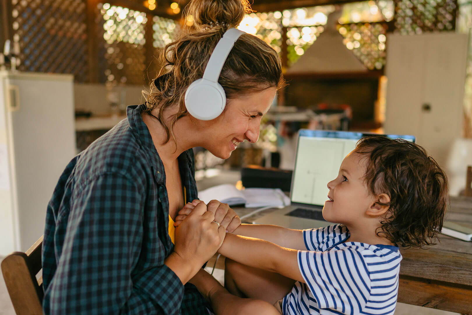photograph of woman wearing headphones smiling and holding hands face to face with child in lap