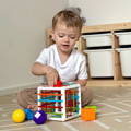 Little boy playing on a bedroom carpet and putting a ball in a Montessori Shape Block.