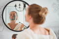 woman applying a face mask in front of the mirror for dewy, glowing skin