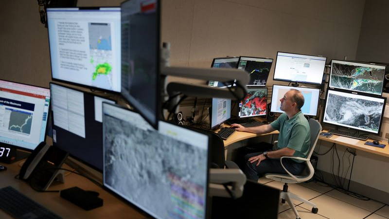 A man looking at hurricane formations on various screens.