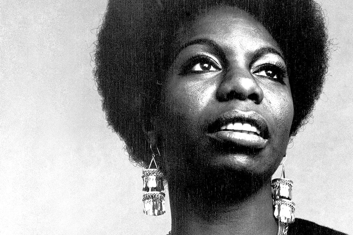 Black and white image of nina simone, wearing large earrings and her hair in an afro, looking to the distance.