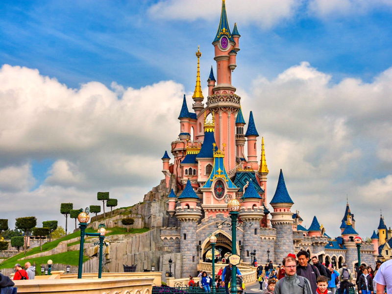 Le château emblématique de Disneyland Paris avec ses tours roses et bleues sous un ciel nuageux