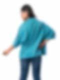 A woman wearing a loose teal top with wide sleeves, viewed from the back, paired with jeans on a white background, showcasing a relaxed casual style.