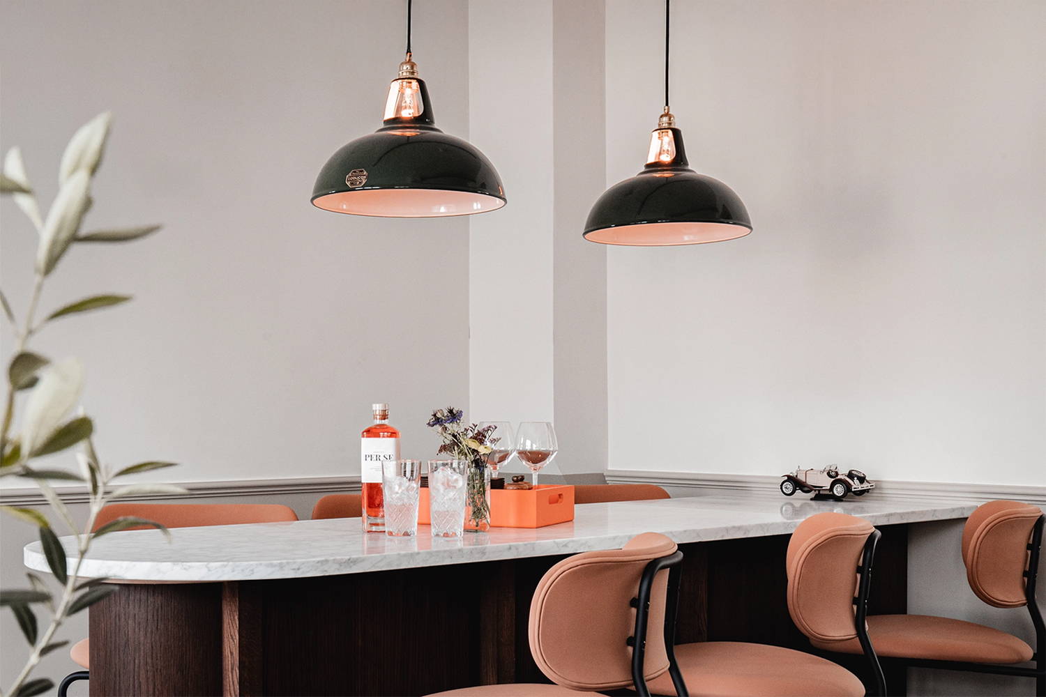 Two large Green Coolicon Pendant lampshades hanging above a bar island inside a restaurant with white walls. 