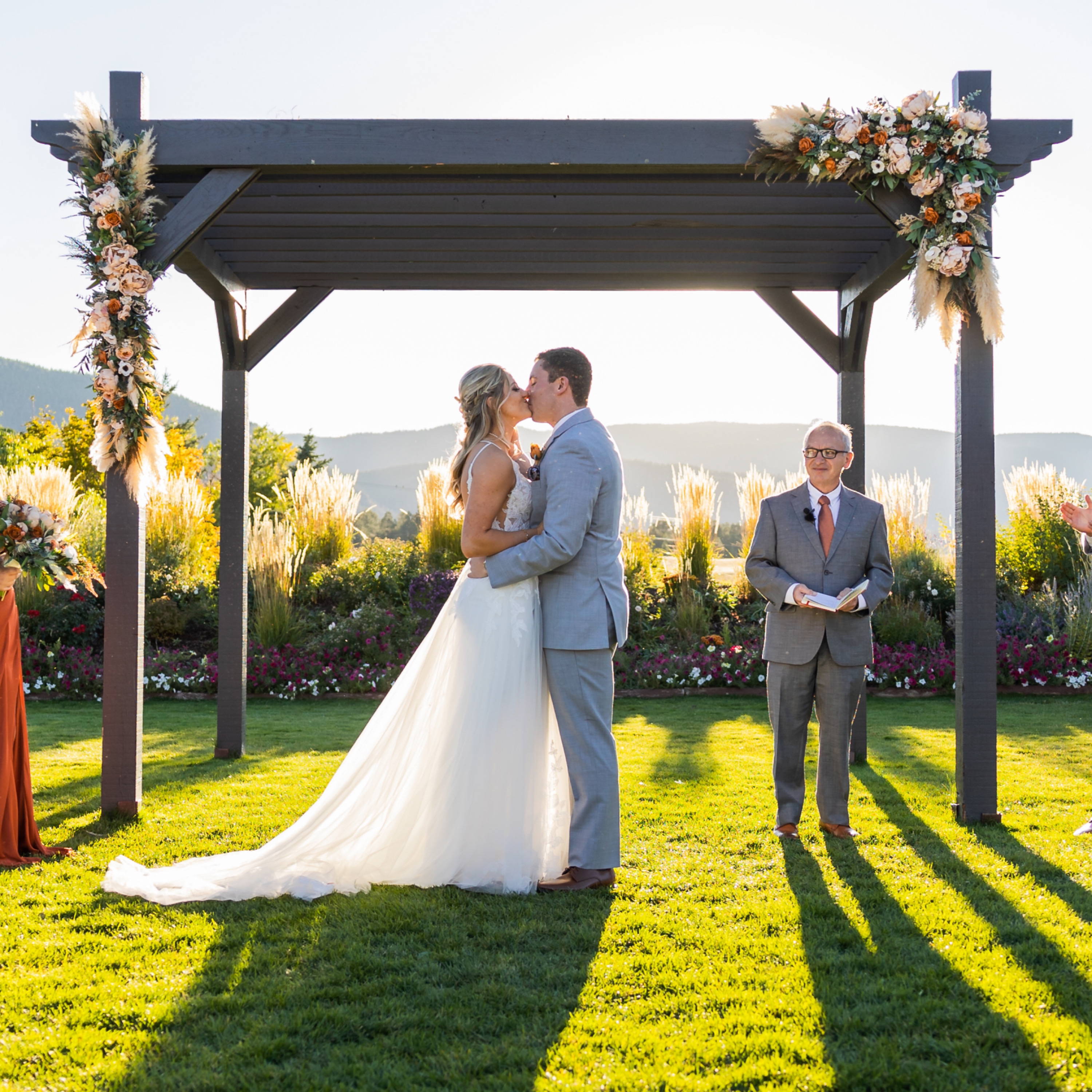A couple shares their first kiss as husband and wife under a pergola decorated with 2 fall wedding floral swags
