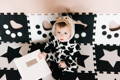 Baby in a cow costume sitting on a black-and-white sensory play mat with geometric shapes.