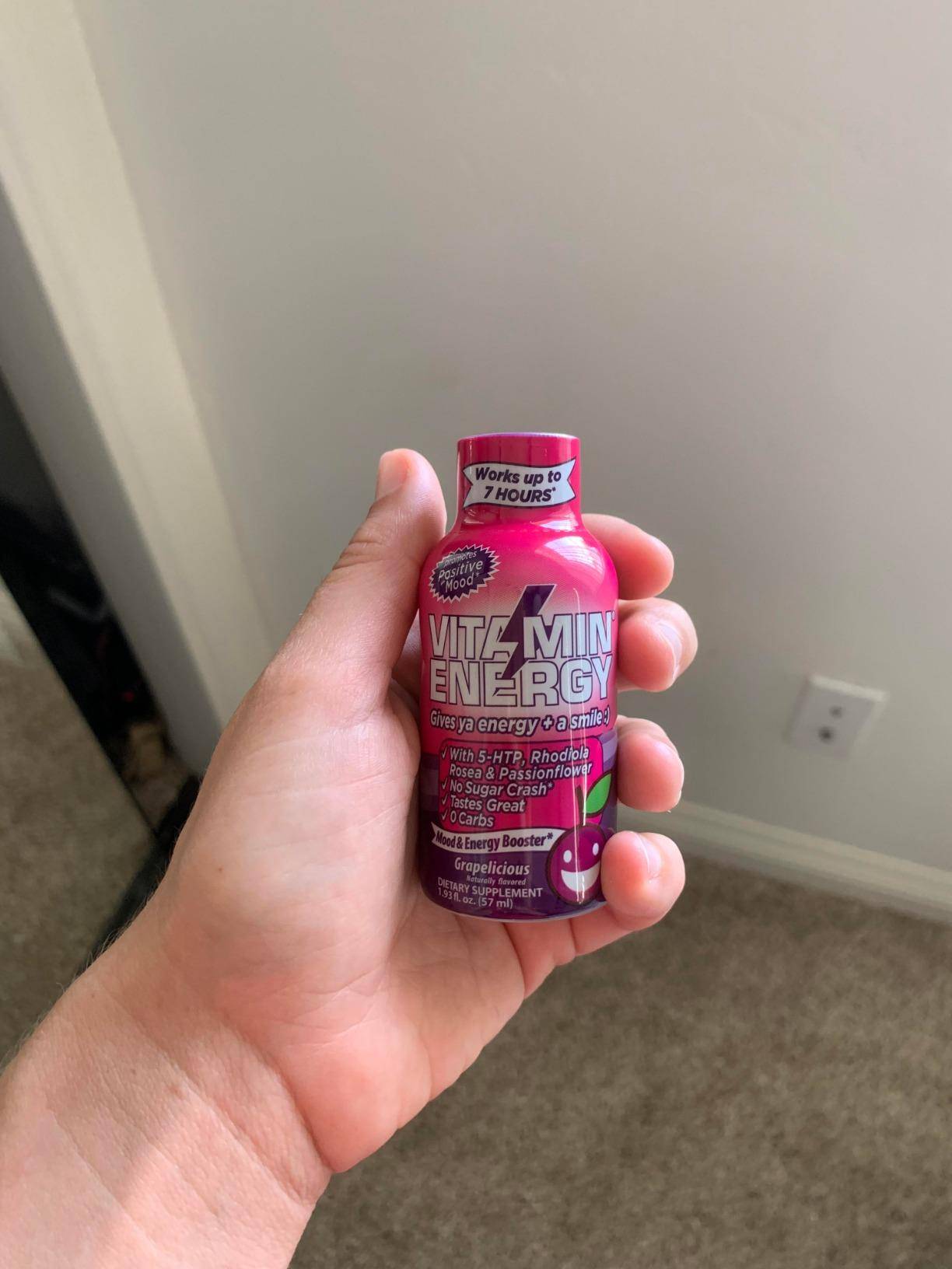 A hand holding a bottle of Vitamin Energy drink labeled 'Grapelicious.'