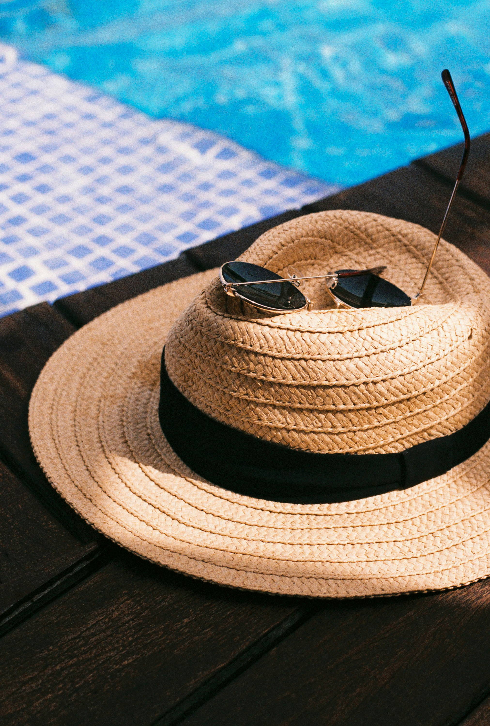 A straw hat with sunglasses next to a blue pool.