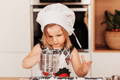 Little girl with a chef's hat making a cookie dough. 