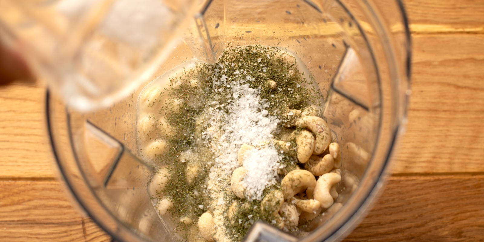 Blender containing cashews, lemon juice, apple cider vinegar, garlic clove, dill, onion powder, and salt & pepper.