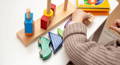 A colorful wooden Montessori toy on a white table and little hands toddler hands playing with it.