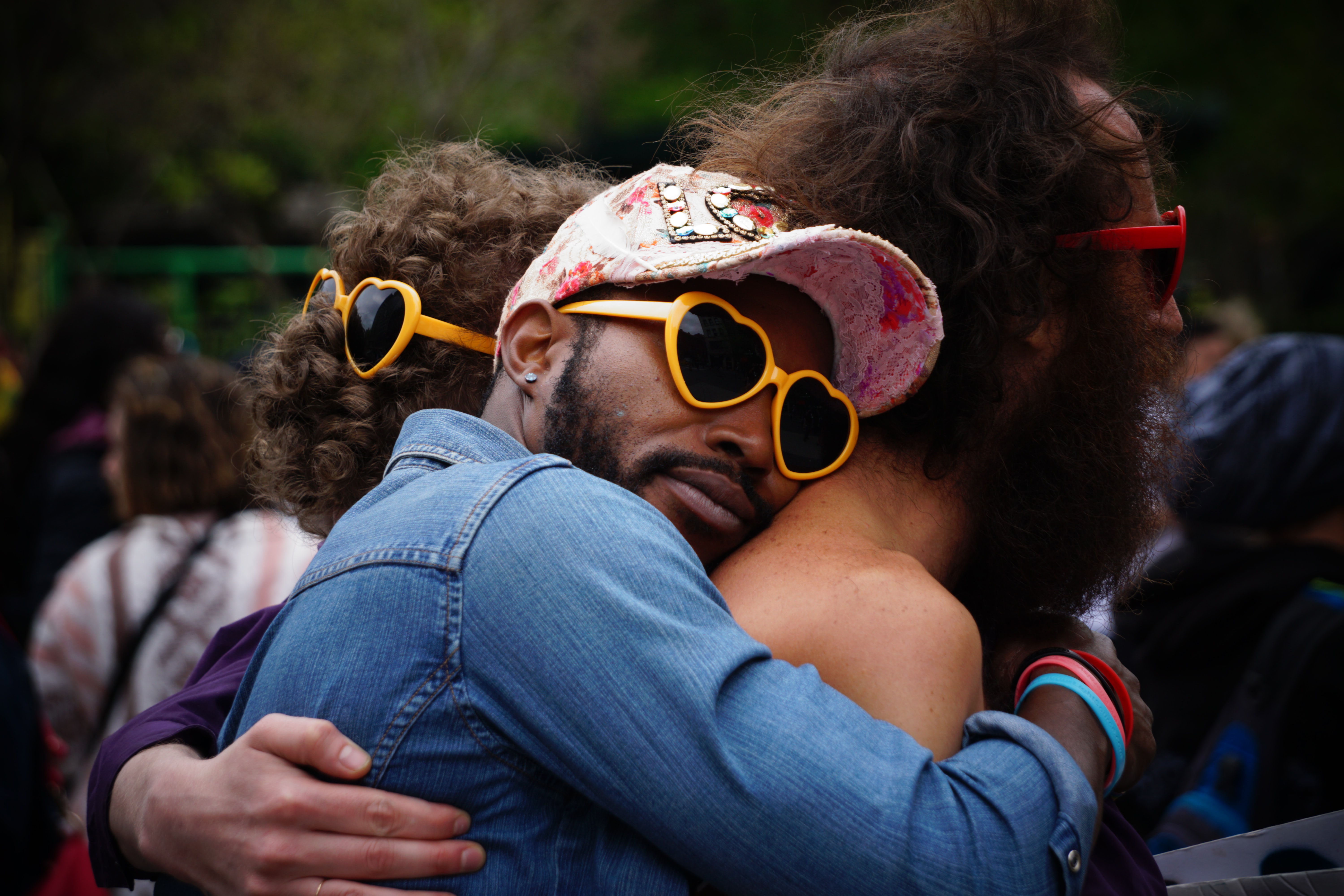 A group of multi ethnic men are in a group hug while wearing heart shaped sunglasses.