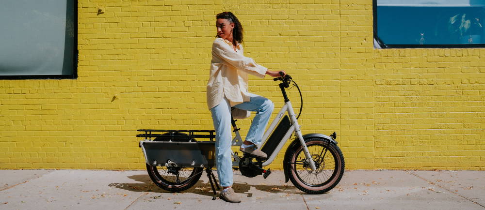 a woman on a white specialized cargo bike in front of a yellow brick wall