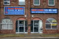 A photograph showing the brick exterior and blue store signs of South Windsor School of Music.