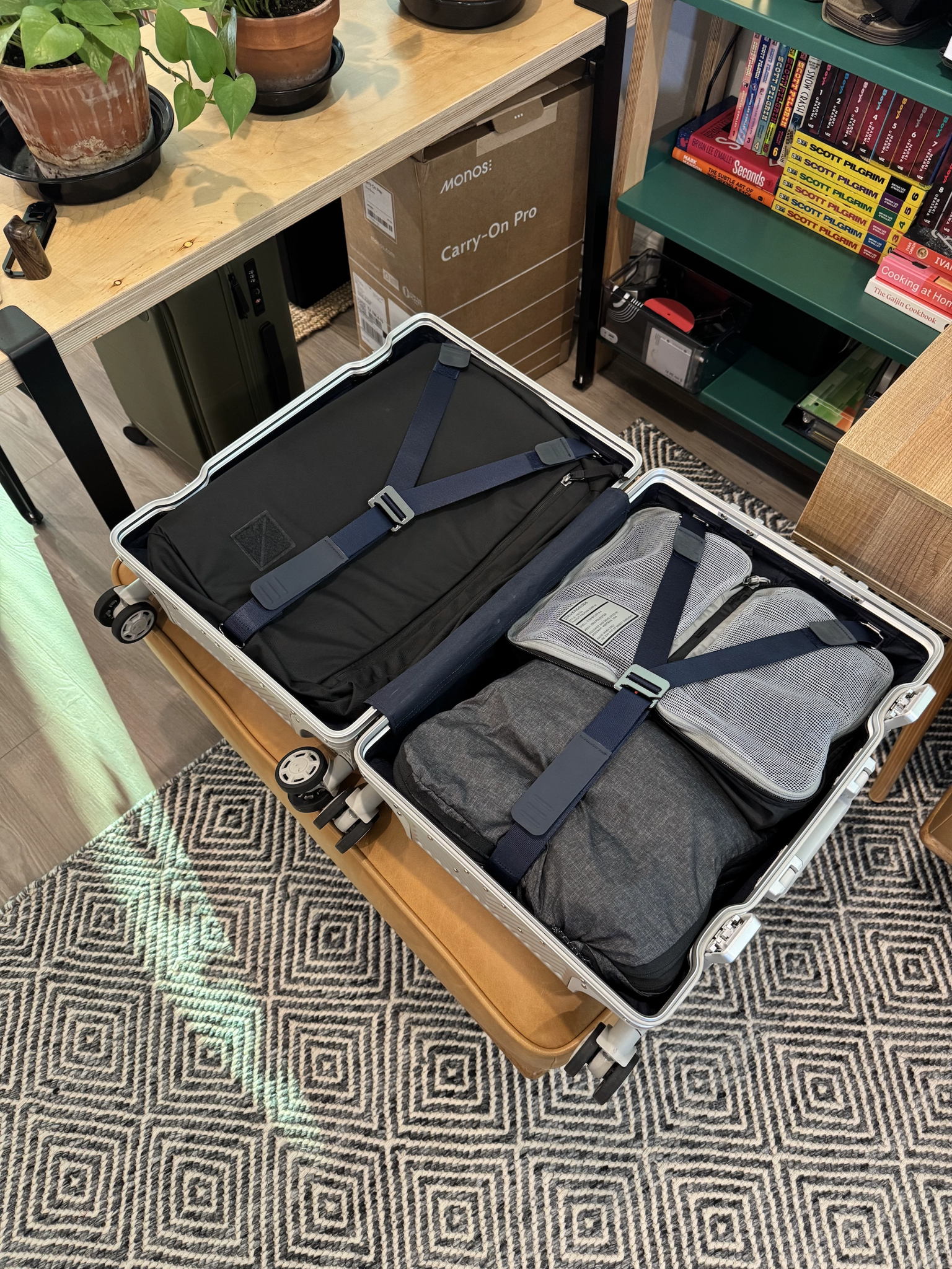 Open rolling suitcase on a bed, one side packed with neatly folded clothes including socks, underwear, t-shirts, pants, and a belt, the other side holding an empty duffel bag. The room appears tidy and well-lit, creating a calm and organized atmosphere. No visible text in the image.