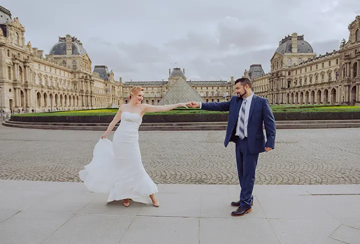 Un moment enchanteur de deux jeunes mariés se tenant en face du Louvre, avec leur robe blanche et leur costume bleu.