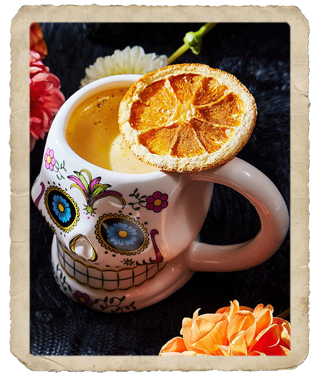 Stylized calavera mug with prepared cocktail and decorating dry orange slice, sided by flowers.