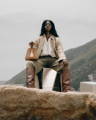 Black female model holding a NOIRANCA handbag Grace Mini in Brown, sitting on a metallic cube