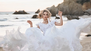 Une mariée se tenant sur la plage, portant une robe de mariée blanche, avec les vagues de l'océan en arrière-plan.