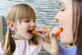 Mother and daughter feeding each other with carrots.